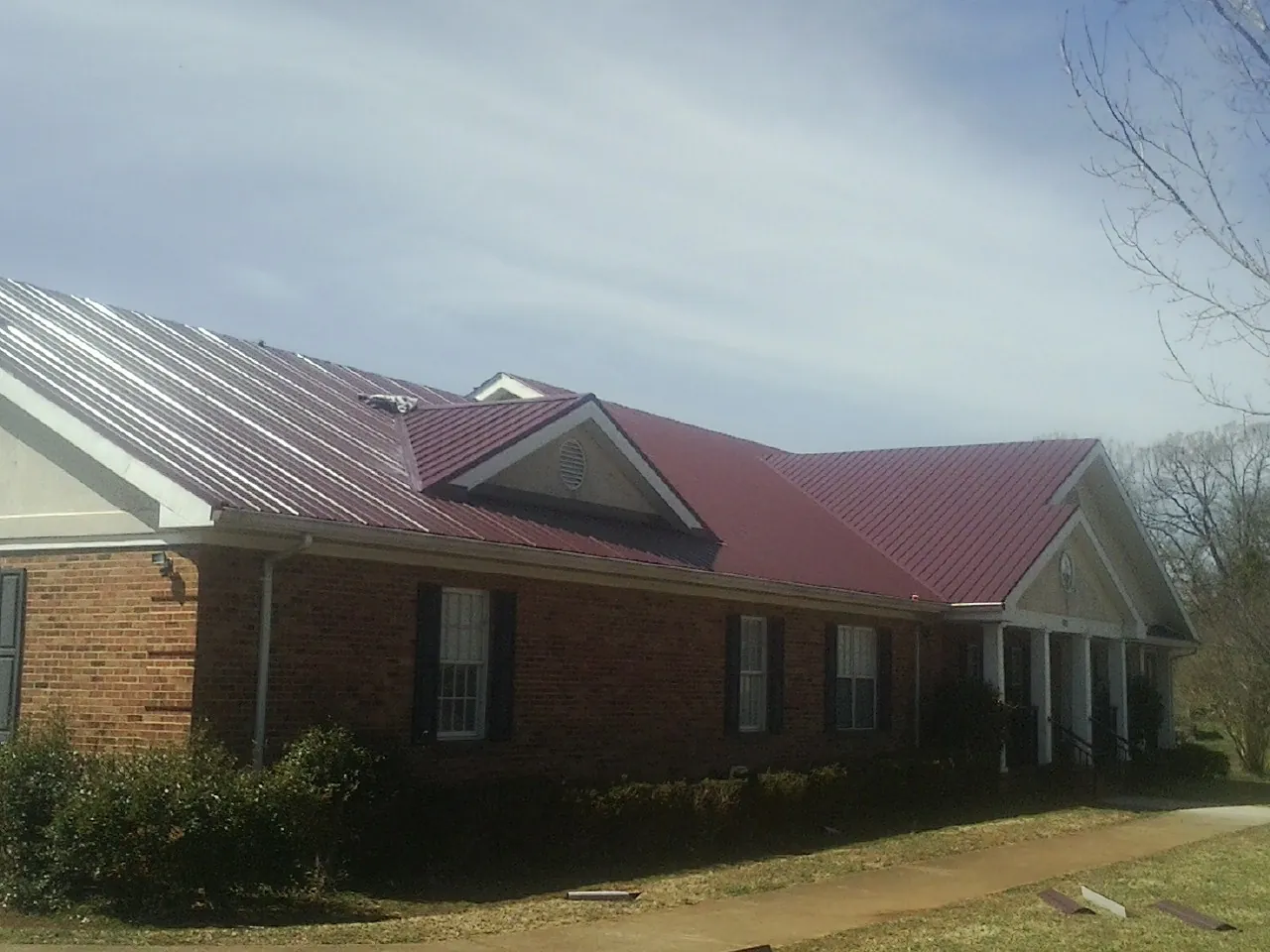 Red metal roof with gabled entries on a long brick building, from a Hail Damage Roof Repair job in Sunman