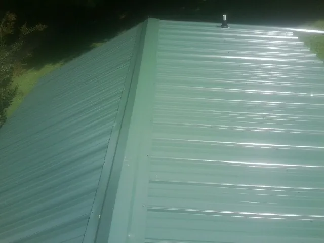 New green metal panels meeting at the ridge of a roof — Flat Roof Repair work by our crew in Sunman