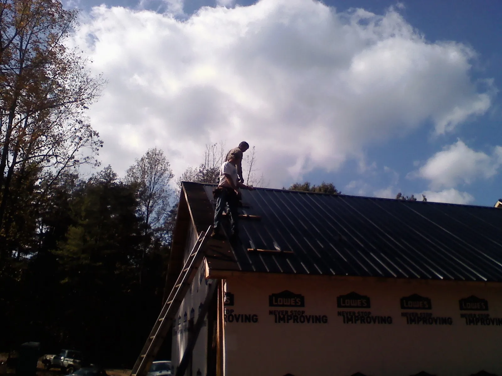 Roofer fastening dark metal panels high against a cloudy sky, from a Roof Inspection job in Sunman