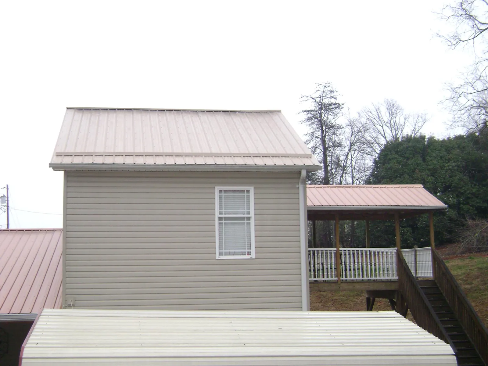 Tan metal roofs on a two story addition and attached porch, from a Roof Replacement job in Sunman